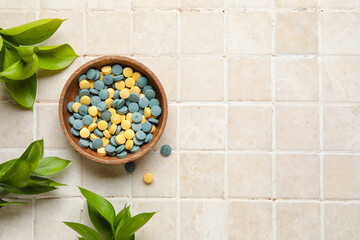 Bowl with pills and plant branches on beige tile background