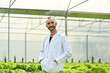 © Prathankarnpap - Positive caucasian male plant researcher, geneticist, biologist in white coat standing among vegetable in industrial greenhouse
