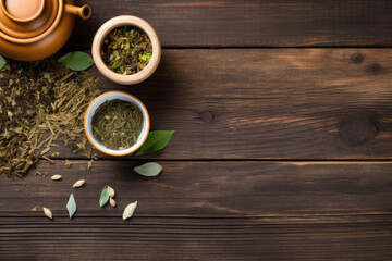 Cup of tea with teapot, organic green tea leaves and dried herbs on wooden table top view with copy space	