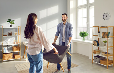 Young couple carrying armchair into their living room. Smiling man and woman moving into new apartment, furnishing and remodeling room. House improvement, remodeling concept