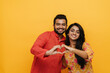 © Drobot Dean - Indian couple showing heart gesture with fingers isolated over yellow background