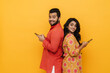 © Drobot Dean - Indian man and woman using mobile phones while standing back to back isolated over yellow background