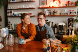 Fototapeta Na ścianę - Man with down syndrome and his female colleague smiling while standing at counter in coffee shop