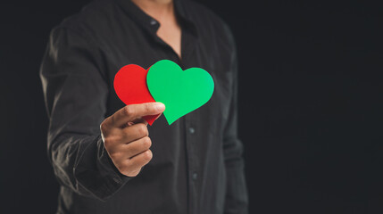 Close-up of hand holding green and red hearts shape symbol while standing on a black background