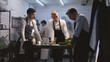 © Framestock - Adult chef cook with employees standing by kitchen desk and discussing quality of products. The cook prepares dish at background. Concept of teamworking at restaurant kitchen. Dolly shot. Slow motion