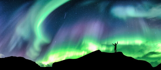 Wall Mural - aurora borealis glowing over silhouette hiker standing on the mountain in the night sky