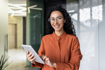 Wall Mural - Portrait of successful hispanic woman inside office at workplace, businesswoman smiling and looking at camera, female worker holding tablet computer.