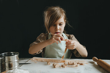 Wall Mural - Father and daughter in aprons holding dough cut into strips on a white table against a dark wall