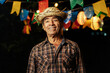 © kleberpicui - Senior man celebrating the Brazilian Festa Junina. Portrait of a man wearing typical clothes and a straw hat under the decoration of pennants and lights from the traditional June festival in Brazil.