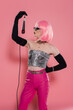 Side view of trendy drag queen in sunglasses holding microphone on pink background.