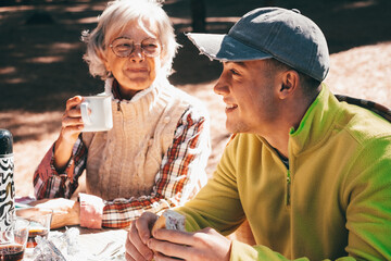 Sticker - Family Couple Bonding Enjoying Together Outdoors Excursion in Mountain Grandma and Grandson Sitting in the Woods Picnic Area with Food and Drink