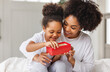 © JenkoAtaman - happy mother's day. african american baby daughter giving  gift box to her mom for holiday at home