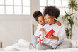 © JenkoAtaman - happy mother's day. african american baby daughter giving  gift box to her mom for holiday at home