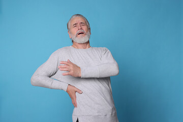 Wall Mural - Senior man suffering from pain in back on light blue background, space for text. Arthritis symptoms