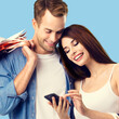 © vgstudio - Love, holiday sales, shop, retail, consumer concept - happy couple with shopping bags, looking at mobile phone. Sky blue background. Square composition image.