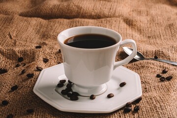 Sticker - Close-up image of a white coffee cup with a saucer surrounded by coffee beans