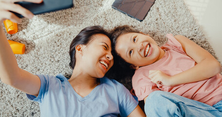 Wall Mural - Asian toddler little girl daughter with mother use smartphone take photo or video call on carpet floor having fun, happy in living room at home. Family spend time together, Creative lifestyle concept.