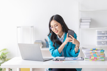 Wall Mural - Business Asian woman hold phone and use laptop at the workplace. Project stats financial data sales charts on laptop and cellphone Asian finance concept
