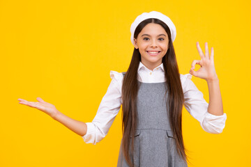 Poster - Close up portrait of teenager child girl showing at copy space, pointing to ads advertising, isolated over yellow background. Mock up copy space. Happy face, positive and smiling emotions.