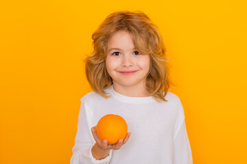 Wall Mural - Kid with orange in studio. Studio portrait of cute child hold orange isolated on yellow background.