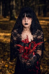 Wall Mural - Vertical portrait of a scary corpse bride holding red flowers in the autumn forest