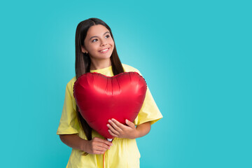 Poster - Valentines day and kids concept. Teenage girl in yellow dress with red heart-shaped balloon over blue background. Happy girl face, positive and smiling emotions.