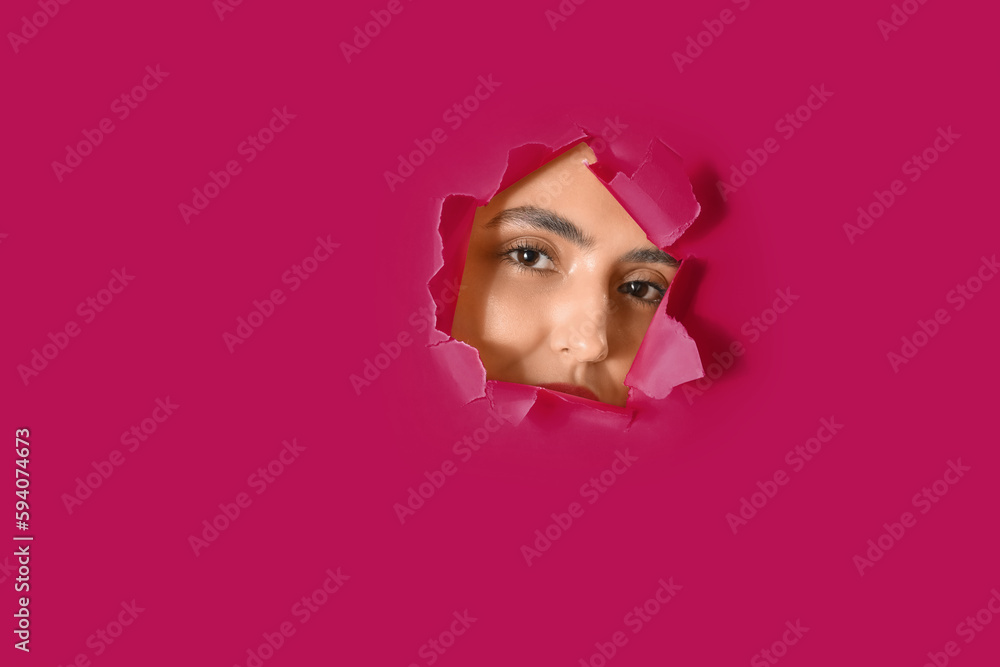 Young woman visible through hole in pink paper