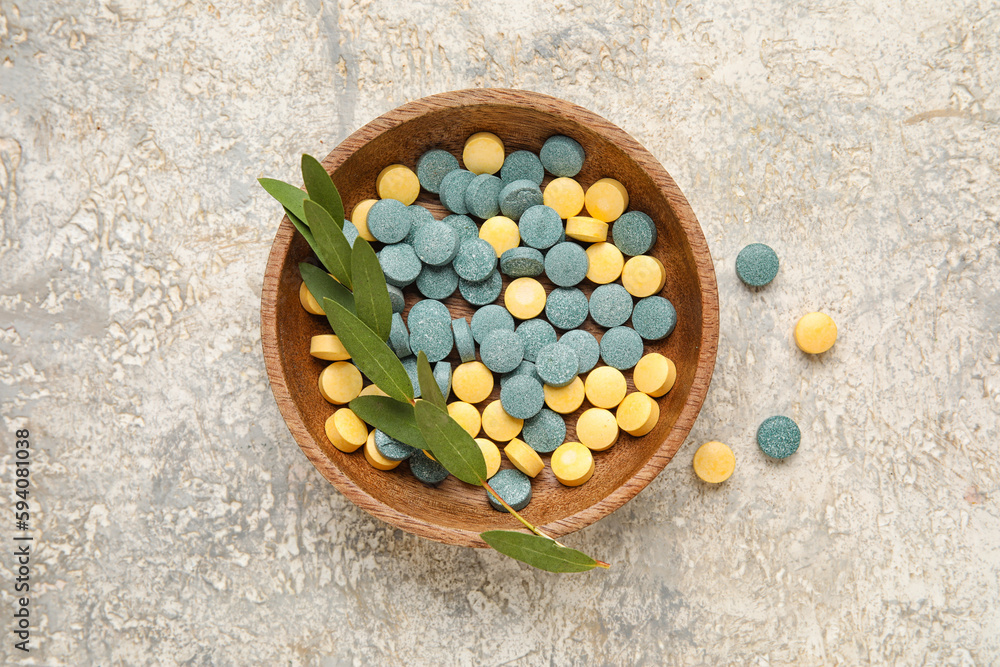 Bowl with pills and plant branch on grunge background