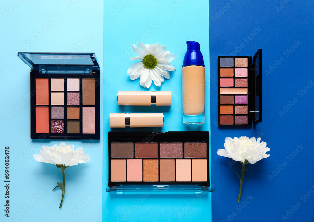 Eyeshadows with lipsticks, makeup foundation and flowers on color background