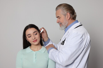 Wall Mural - Doctor dripping medication into woman's ear on light grey background