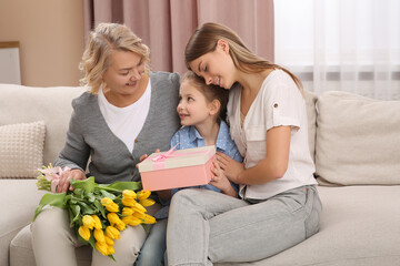 Wall Mural - Little girl congratulating her mom and granny with flowers and gift at home. Happy Mother's Day