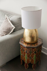 lamp with gold base on moroccan inspired side table next to grey sofa in apartment living room