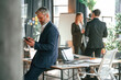 © standret - Man is leaning on the table. With smartphone in hands. Group of business people are working in the modern office