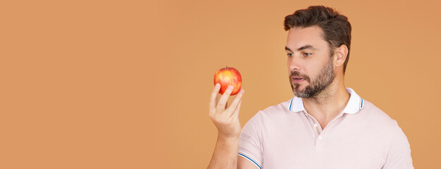 Middle aged man bitting apple, healthy lifestyle. Man holds a fresh apple studio portrait on beige isolated background. Healthy food. Fruit for healthy teeth. Man holding apple. Banner, copy space.