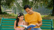 © Knot9 Images - Caring dad reading out an interesting story to his little child sitting outdoors. Medium shot of a father-daughter duo spending some good moments together in a park - family love concept