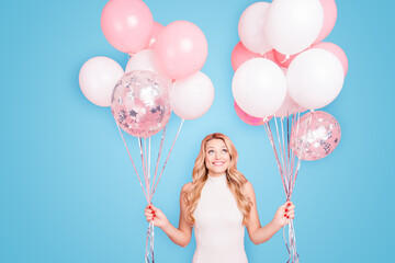 Portrait of trendy cheerful elegant girlfriend having many white air balloons in two hands looking up enjoying ballons isolated on pink background