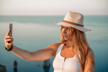 Selfie woman in hat, white tank top and shorts makes selfie shot mobile phone post photo social network outdoors on sea background beach people vacation lifestyle travel concept.