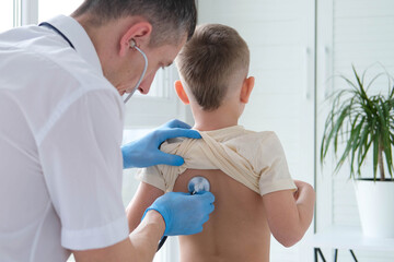 The doctor listens to the breathing of a little boy through a stethoscope. Pediatrician with stethoscope listens to the lungs of a child with bronchitis and cough