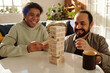 © pressmaster - Happy African American teenage girl playing jenga with her foster dad at table in the living room