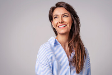 studio portrait of attractive woman wearing shirt and laughing while sitting at isolated grey backgr