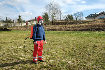 Wall Mural - Man gardener wearing protective clothing and full face respirator mask with dust filters and backpack, knapsack, shoulder-mounted battery sprayer. PPE. Safety precautions. Equipment for pest control