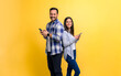 © Moon Safari - Portrait of smiling couple dressed in casuals using smart phones against yellow background. Cheerful young man and woman standing back to back and messaging online on social media