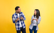 © Moon Safari - Young couple laughing cheerfully and playing video game over smart phones while standing against yellow background. Excited man and woman dressed in casuals competing and looking at each other