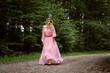 © Ionut Dragoi/Wirestock Creators - Young blonde woman in a pink long dress walking barefoot in the forest.