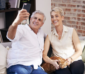 Sticker - Snapping some family portraits. a mature couple taking selfies while relaxing with their pet cat on a sofa at home.