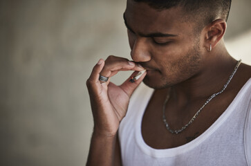 Wall Mural - Getting high just to get by. a young man smoking a marijuana cigarette against an urban background.