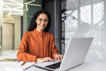 Wall Mural - Young beautiful hispanic woman working inside modern office, businesswoman smiling and looking at camera at work using laptop