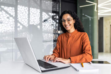 Wall Mural - Young beautiful hispanic woman working inside modern office, businesswoman smiling and looking at camera at work using laptop