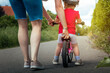 Mutter übt mit Kind das einen Fahrradhelm tägt auf der Straße das Fahrrad fahren bei strahlender Sonne