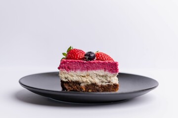 Poster - Delicious slice of strawberry-topped cheesecake on a matte dark grey plate on a white background